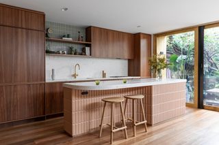 Rich wood kitchen cabinets with rounded island tiled with large pink finger tiles, topped with white stone countertop