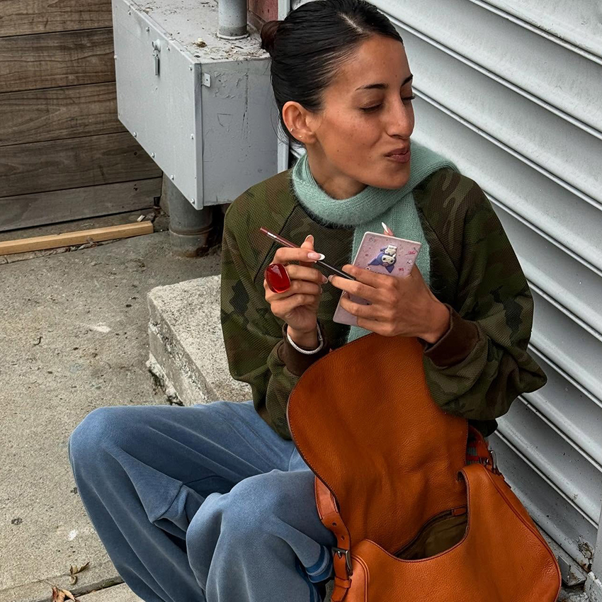 a woman wearing a camouflage jacket, brown leather bag, and blue jeans 