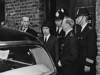 Bill Wyman is escorted from West Ham Court by policemen after appearing on charges relating to an incident at an all night filling station, London, July 22nd 1965