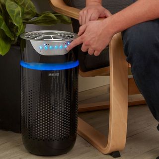 HoMedics TotalClean 5-in-1 Tower Air Purifier in black being used by person sitting in chair