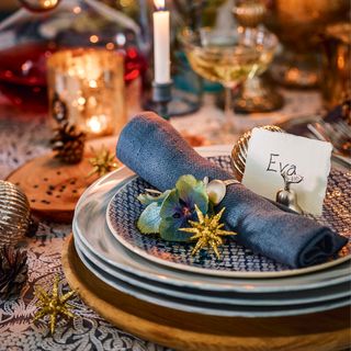 blue Christmas napkin rolled up and place on blue and white side plate with gold star decorations