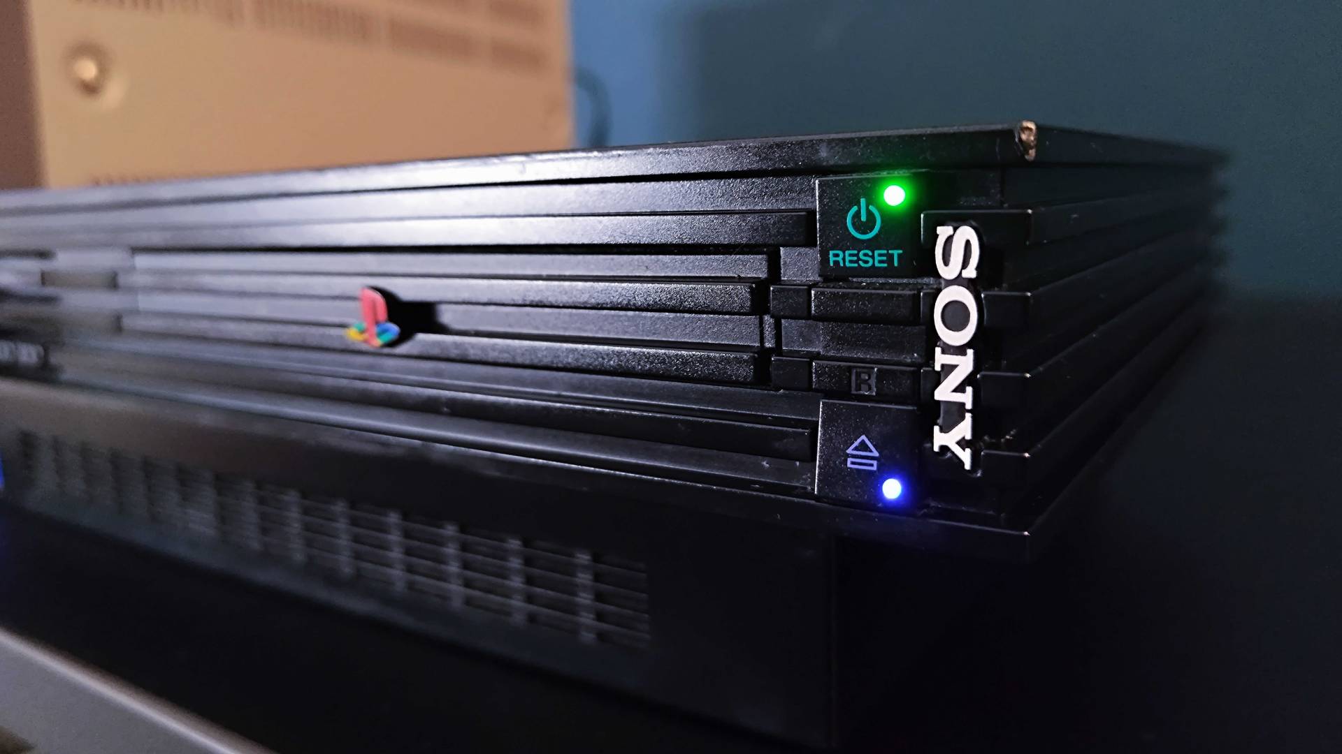 Close up of original PS2 switched on with green reset and blue eject button lights illuminated.
