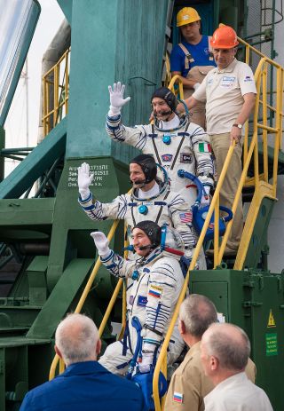 Soyuz MS-13 crew members Aleksandr Skvortsov, Drew Morgan and Luca Parmitano wave from the base of their Soyuz rocket prior to boarding the vehicle on July 20, 2019.