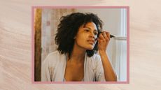 Woman wearing a robe and doing her eyebrows in the mirror, with a pink painted background