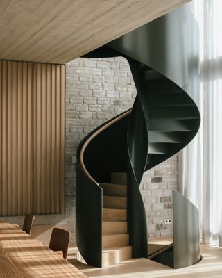 A room with a black spiraled staircase, a wooden dining table, a stone wall and wooden flooring.