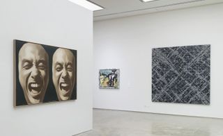 Art exhibition space. Displayed on one wall is a large piece of artwork with 2 identical images of a bald-headed man screaming or shouting. Another wall displays an abstract piece of art of in black and white.