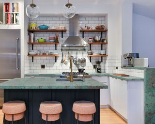 Modern kitchen with green Amazonite Quartzite countertops, white cupboards and white brick tiles splash-back behind stove, bar stools with black metal frames, cork seats, glass hanging pendants above island