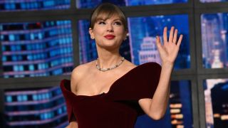 Taylor Swift looking up and waving with her right hand during her entrance on The Late Show with Stephen Colbert.