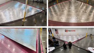 a large triangular sail made of silver foil is unfurled in a hangar as scientists look on