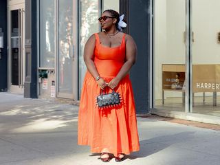 Chichi wears red-orange dress, black slingbacks, blue flower hair scrunchie, and a black spiked bowler bag.