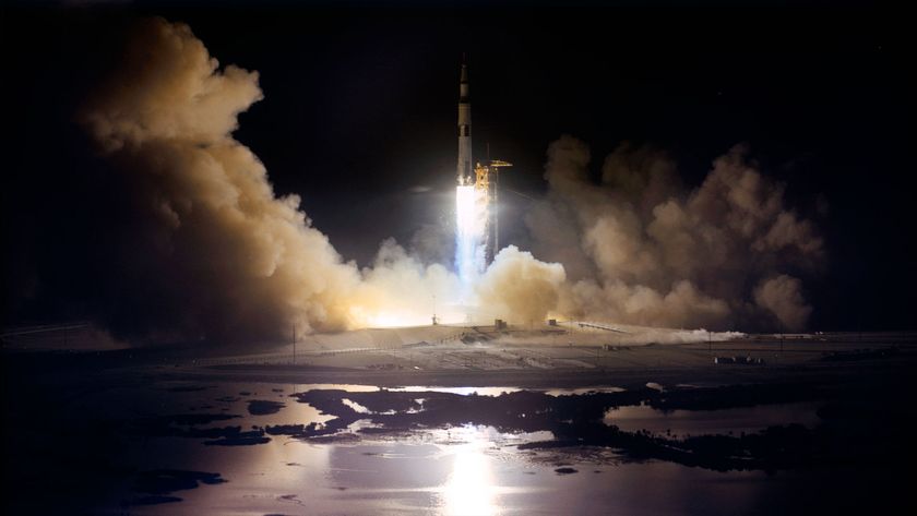 a large white rocket with black stripes lights up the horizon as it lifts off its launch pad at night