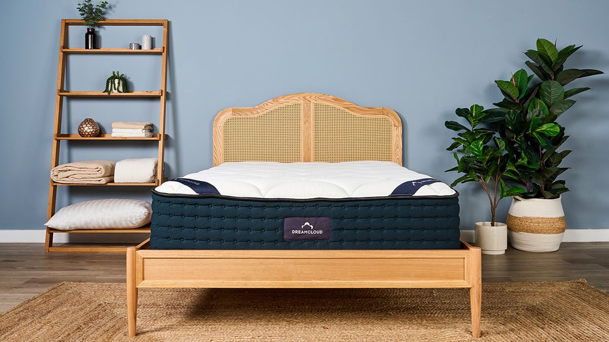 Our review sample of the DreamCloud Luxury Hybrid mattress placed on a rattan bed frame in our blue walled Sleep Lab during test photography