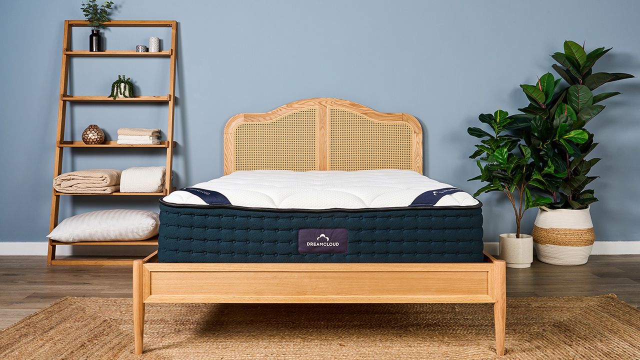 Our review sample of the DreamCloud Luxury Hybrid mattress placed on a rattan bed frame in our blue walled Sleep Lab during test photography
