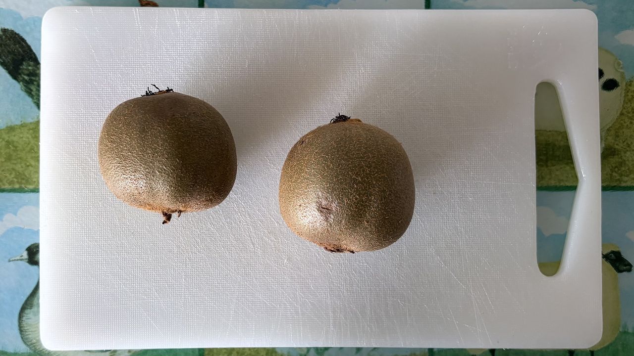 A close up of two kiwis on a white chopping board