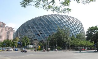 Alternative exterior view of the curved, irregular shaped Phoenix TV building under a clear blue sky. There are trees, buildings and a road with multiple vehicles nearby
