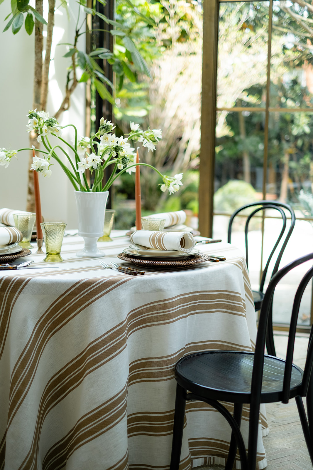 A round dining table with black chairs and a striped table cloth dressing it. The place settings are centred around a small white vase of flowers, and each place setting is decorated with a napkin in a matching print to the table cloth.
