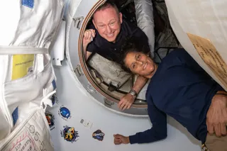 Two astronauts smile in a small circular doorway aboard the International Space Station