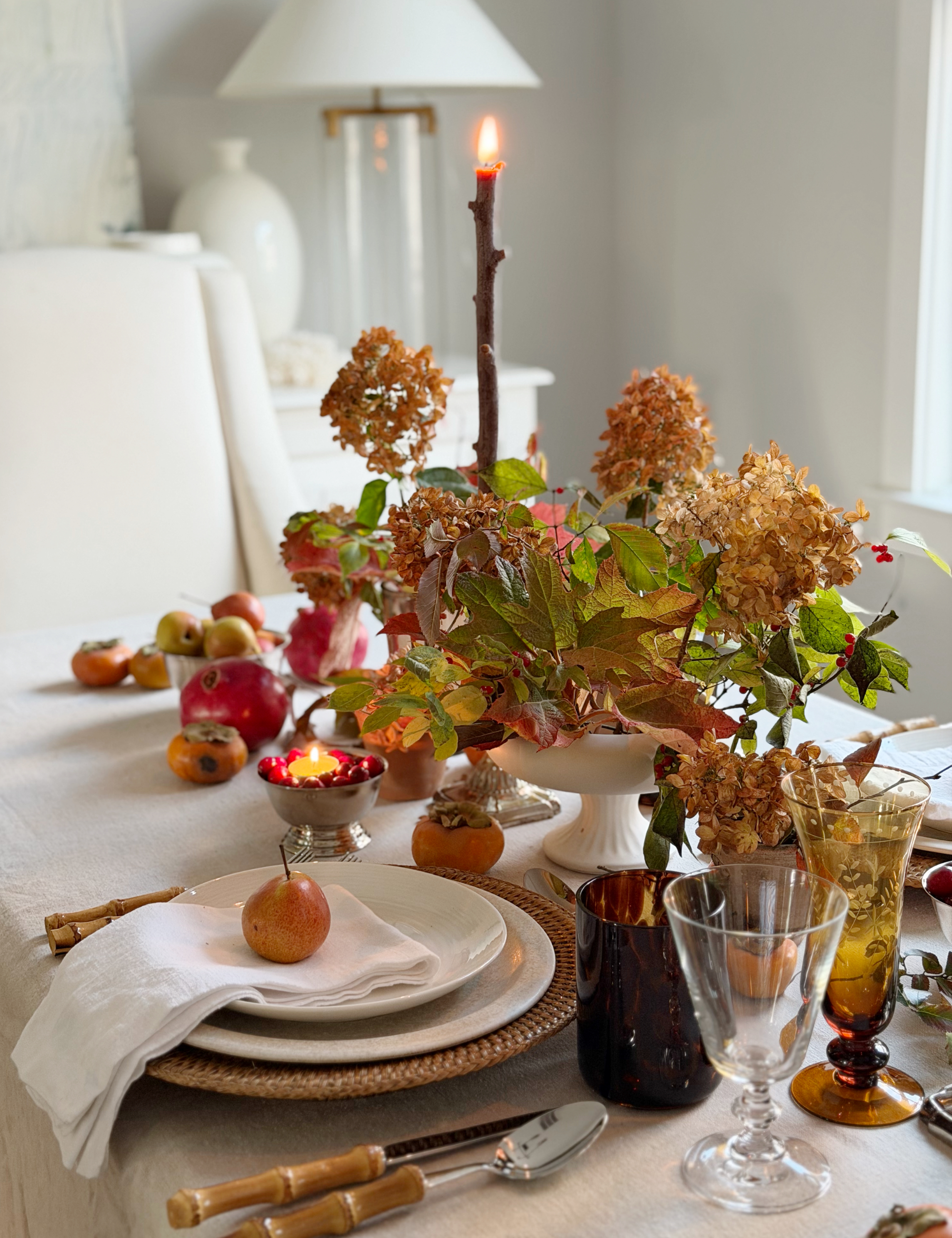 Light, bright fall table setting featuring a woven plate charger, cream dinner plates, bamboo cutlery, and amber wine goblets.