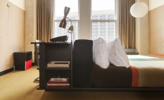 Side view of a black desk against a bed with white pillows
