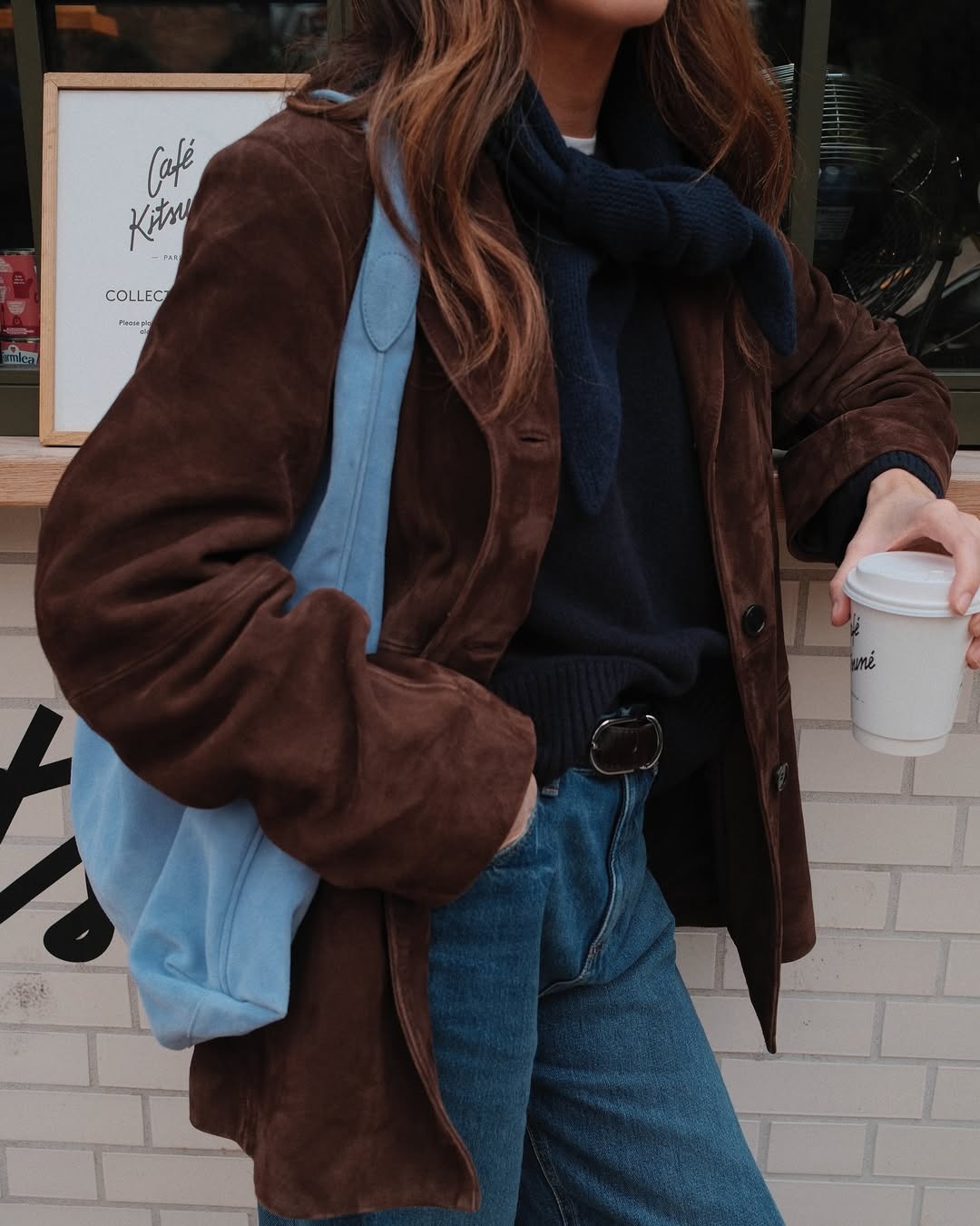 Woman in a dark brown suede blazer and a blue suede bag