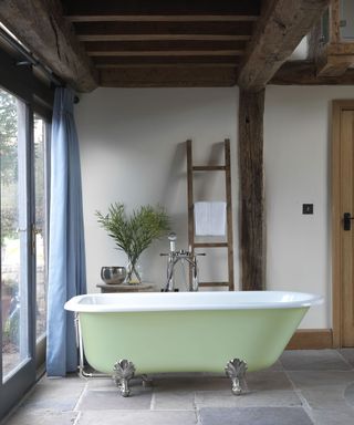 Pastel green freestanding bath tub with wooden storage ladder and beams by Victoria + Albert Baths