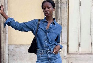 French influencer Sylvie Mus wearing a denim chambray shirt and denim straight-leg jeans and standing on a street in Paris.