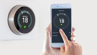 A smart thermostat control panel on the wall next to a phone connected via the app adjusting the temperature