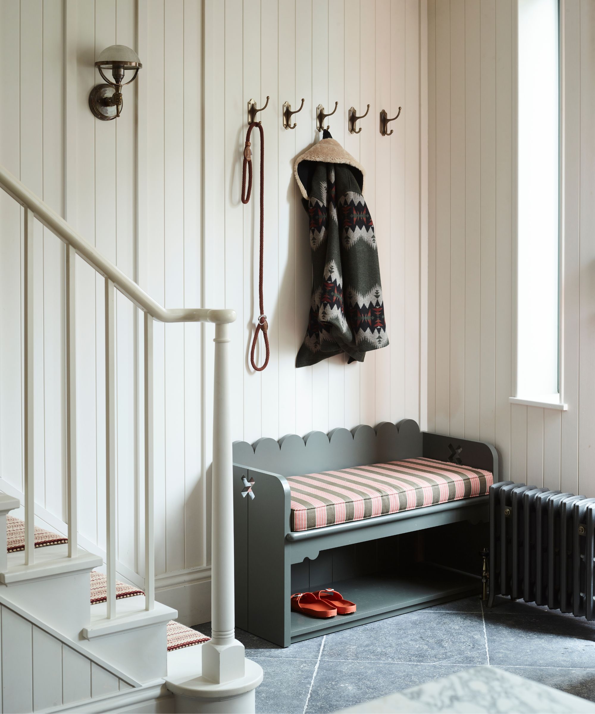 white panelled entryway with white painted staircase and a small boot room area with a bench and coat hooks