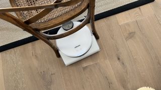 aspirateur robot blanc sous une chaise sur un plancher en bois