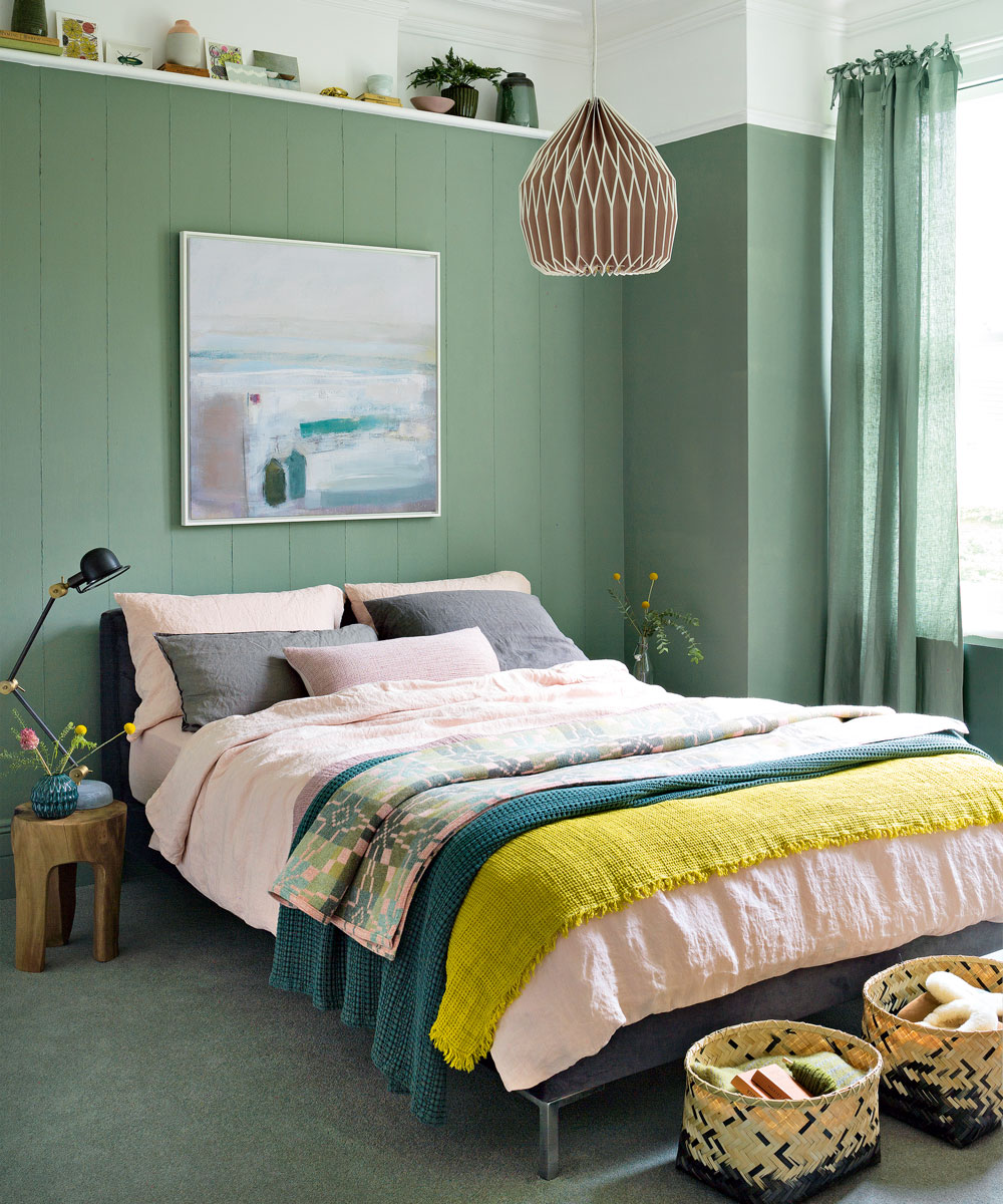 Green bedroom with double bed, colourful cushions and wooden side table.