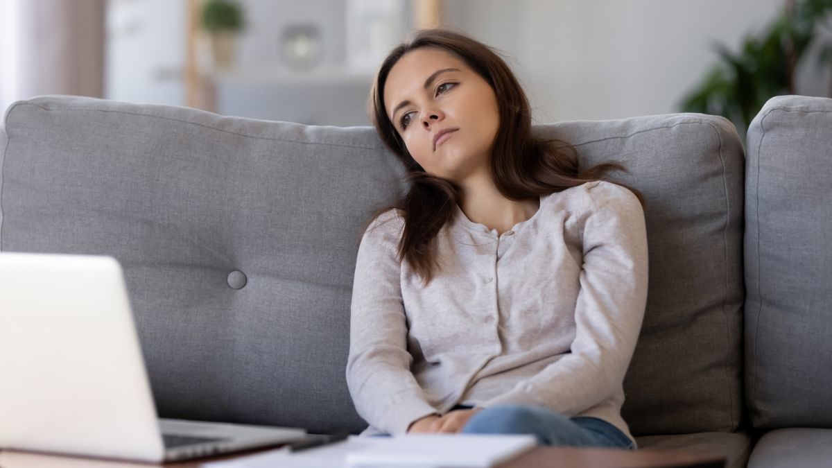 A woman sitting on a couch in front of a laptop looking bored