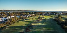 Two holes, the clubhouse and sea pictured from a drone shot of Scotscraig Golf Club