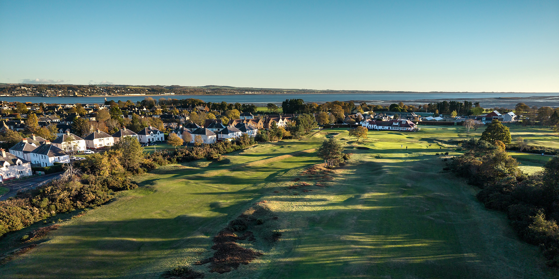 Two holes, the clubhouse and sea pictured from a drone shot of Scotscraig Golf Club