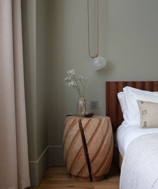 A light green bedroom with a unique wooden nightstand and a hanging light fixture