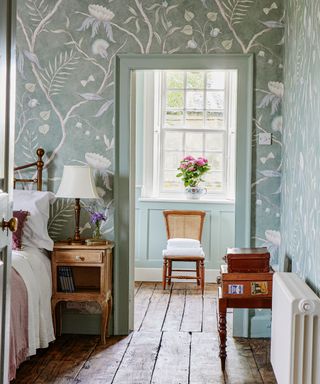 bedroom with pale green floral wallpaper, wooden floor and furniture, painted pale green doorframe