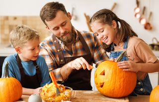 A father with his two children, carving pumpkins for Halloween.
