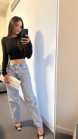 Jordan Gross wearing light-wash jeans, black heels, a black long-sleeve crop top, and a Bottega Veneta Andiamo clutch in white.