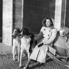 fashion: a woman in a camel hair coat with hood sitting on the bumper of a car, next to her two greyhounds - 1939- Photographer: Sonja Georgi- Published by: 'Die Dame' 04/1939Vintage property of ullstein bild
