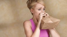 A woman breathes into a paper bag.