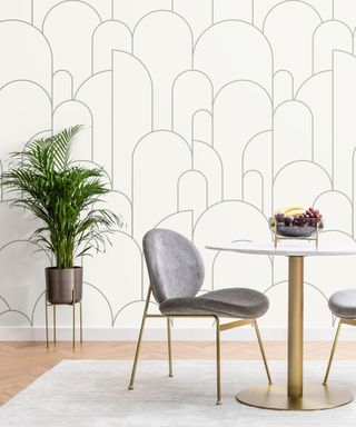 A dining room with a white and gold table, gray chair, plant and geometric wallpaper
