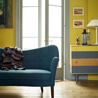 living room paint colours 2023, yellow living room with grey and yellow painted side board, artwork, blue retro style sofa, wooden floor boards
