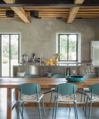 kitchen diner with beamed ceiling, gray walls, stainless steel kitchen island, wooden table and aqua metal chairs