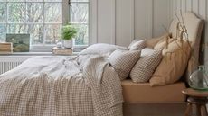 How to sleep better: breathable bedding in calming colors on a bed beside a window with plenty of natural light.
