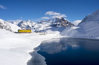 The bright yellow Hotel Portillo in Chile surrounded by snow-covered mountains and Lake Inca