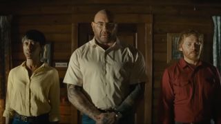 Nikki Amuka-Bird, Dave Bautista, and Rupert Grint stand in a line in the cabin in Knock at the Cabin.