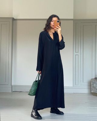 British influencer Marianna Smyth poses for a mirror selfie in a navy satin maxi shirt dress, green Dragon Diffusion and flat black boots