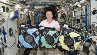 astronaut with three boxes floating on the international space station