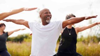 An older black man smiles while practicing yoga