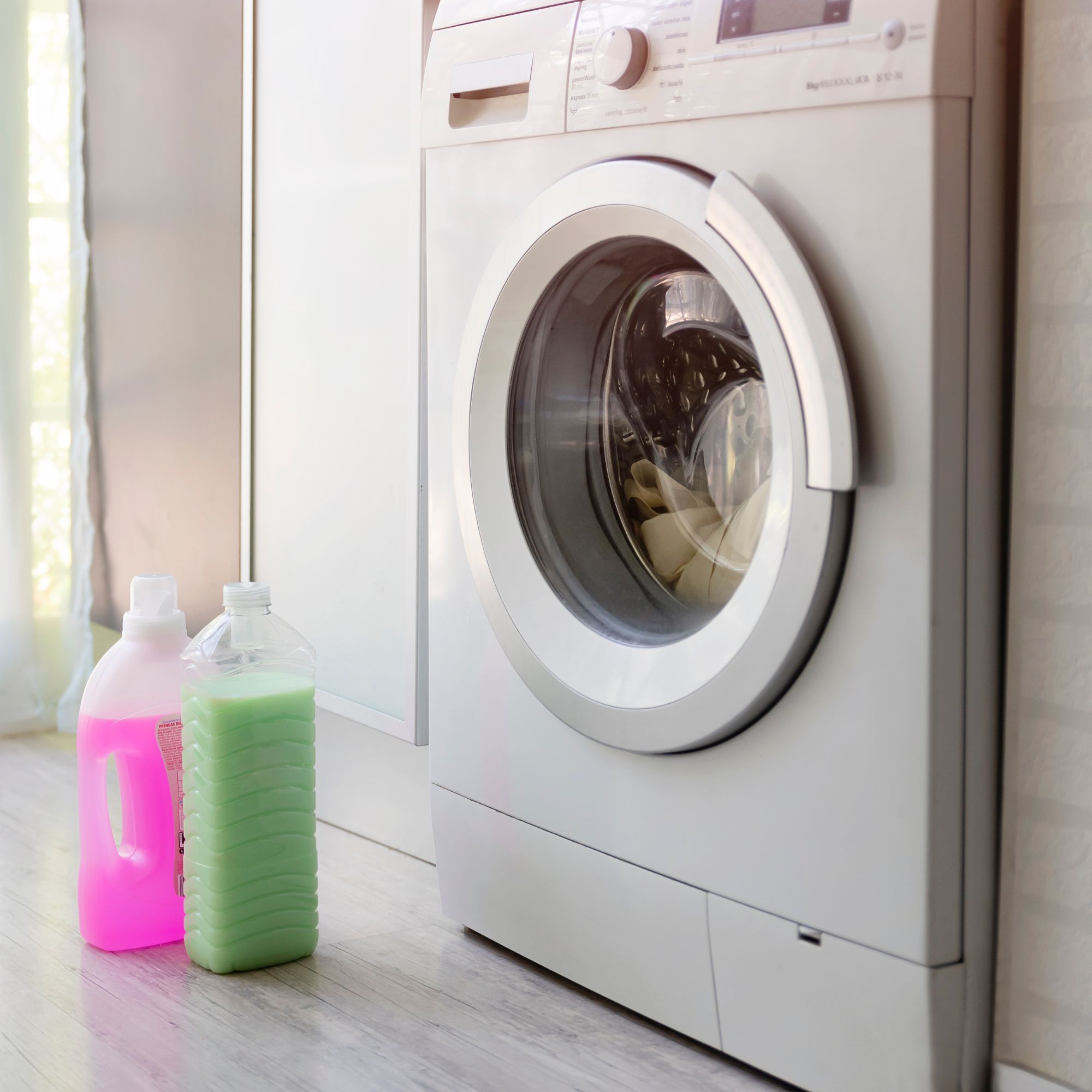 Washing machine in utility room with bottle of detergent and bottle of fabric softener on floor opposite
