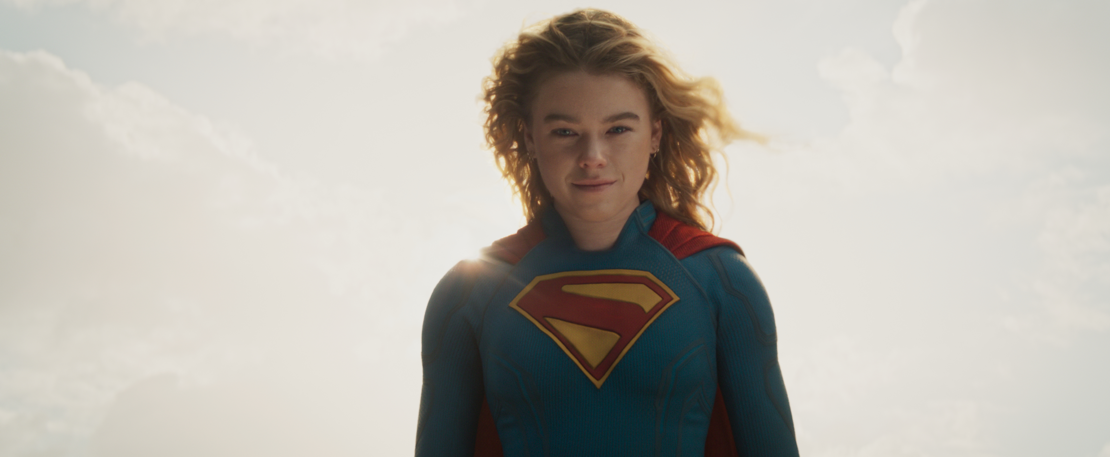 milly alcock as super girl flying in the sky wearing her uniform and smiling in a still from 2026 supergirl
